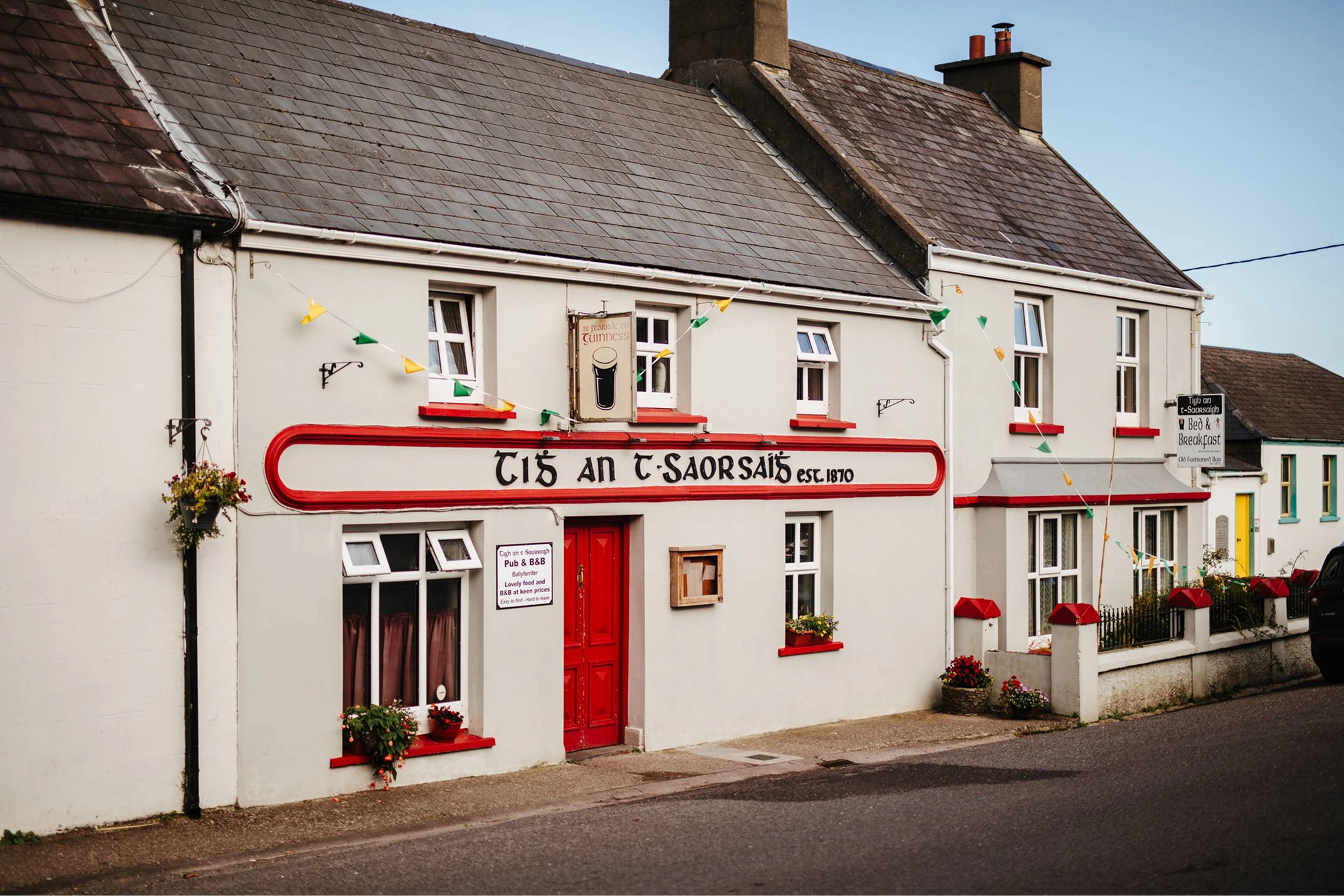 A white-walled Irish cottage with a distinctive red curved signage reading 